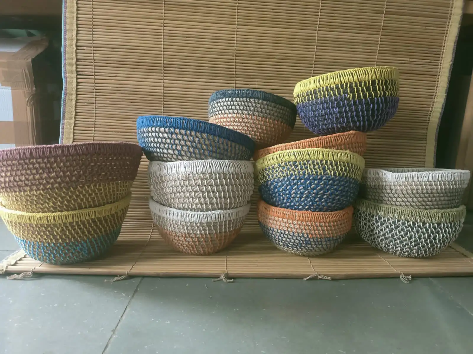 Hand-woven bowls in dyed fibre, stacked on a reed mat