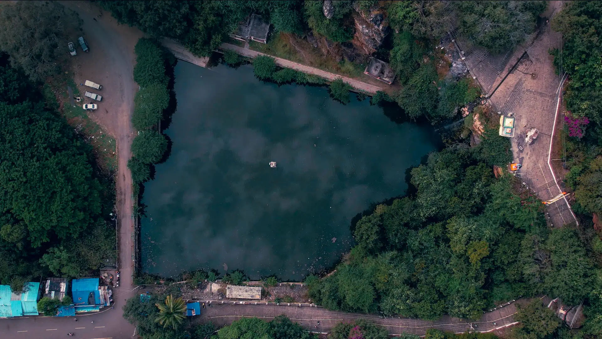 A dark green temple tank at Sogal seen directly from above, ringed by forest