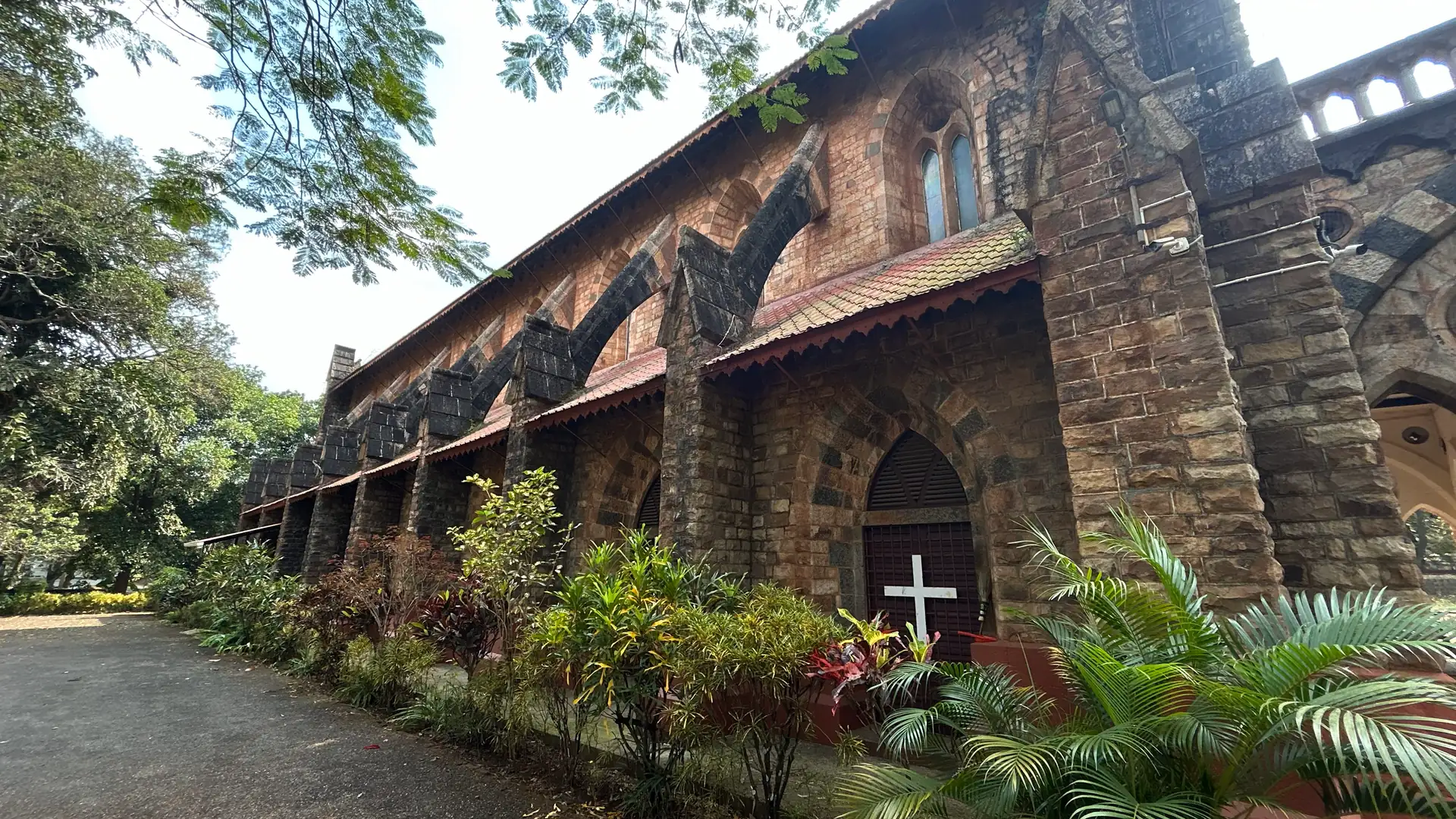 The buttressed laterite flank of St. Mary's Church, Belagavi, its Gothic arches running back into the trees