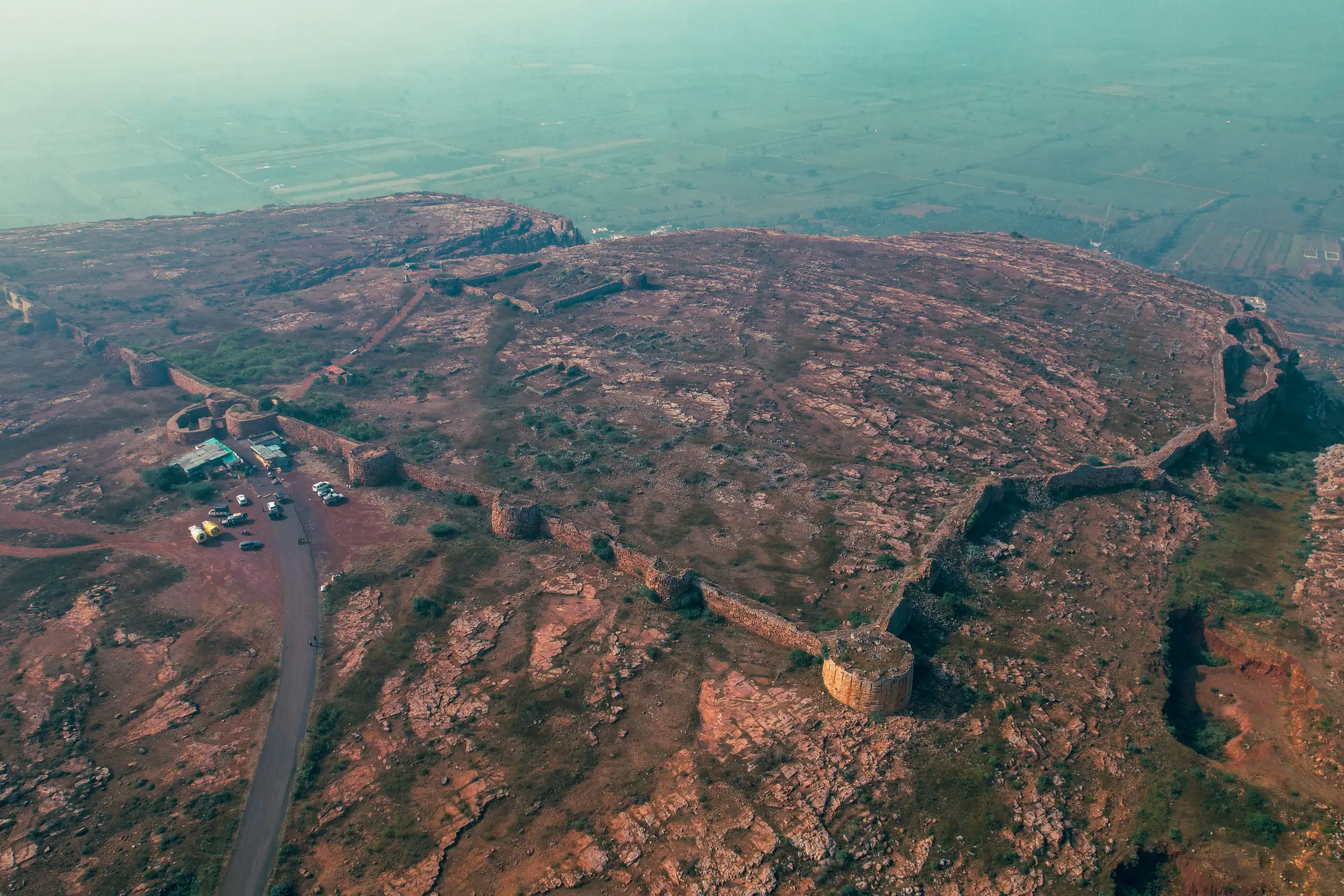 The vast rocky plateau of Savadatti Fort seen from the air, its bastions dissolving into morning haze